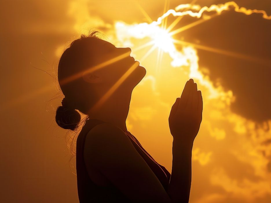 Silhouette of a woman who folds her hands and looks upward to pray.
